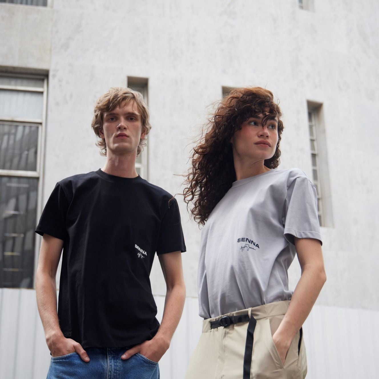 Two people standing against a white building, wearing black and gray t-shirts.