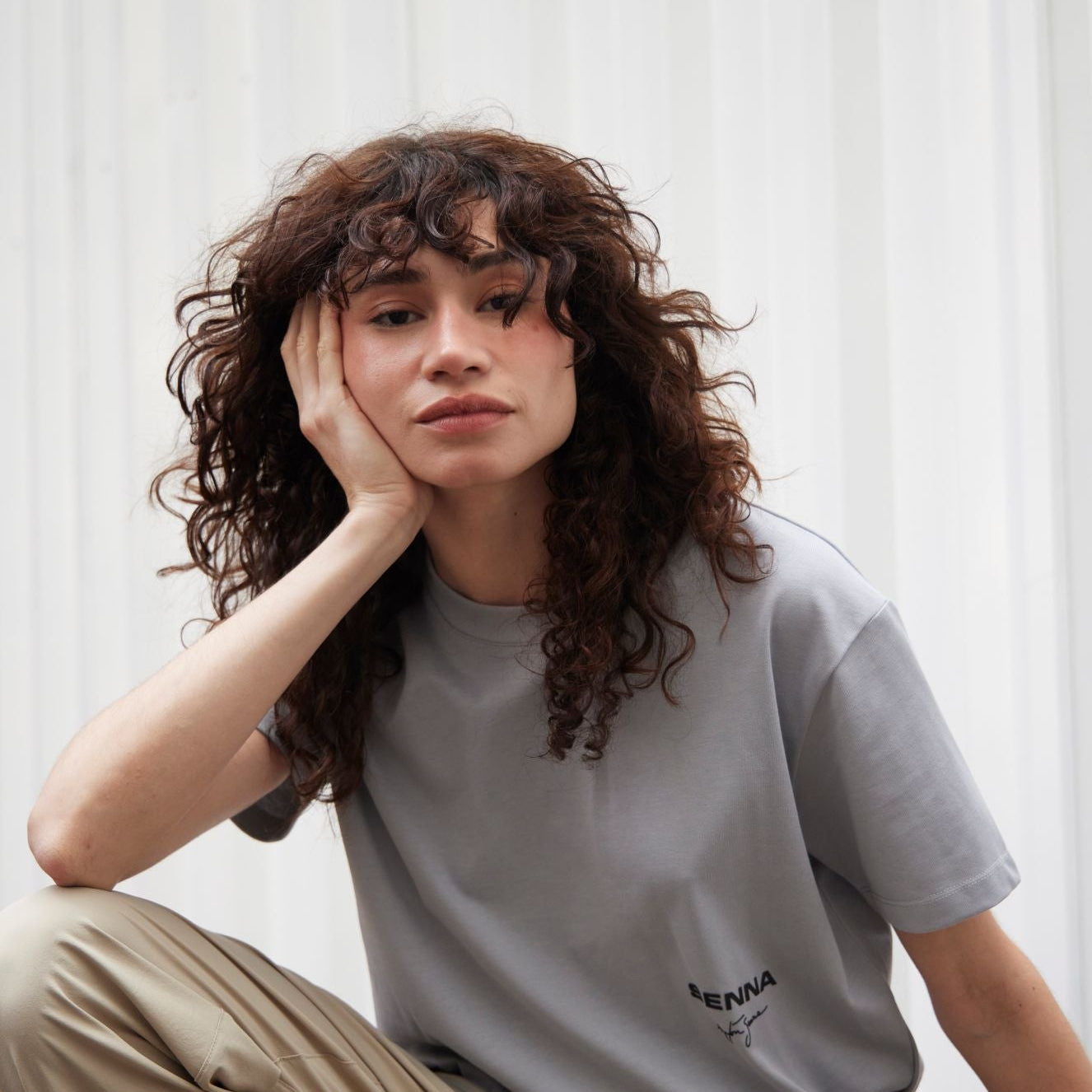 Person wearing a gray t-shirt with text and beige pants sitting on a wooden floor.
