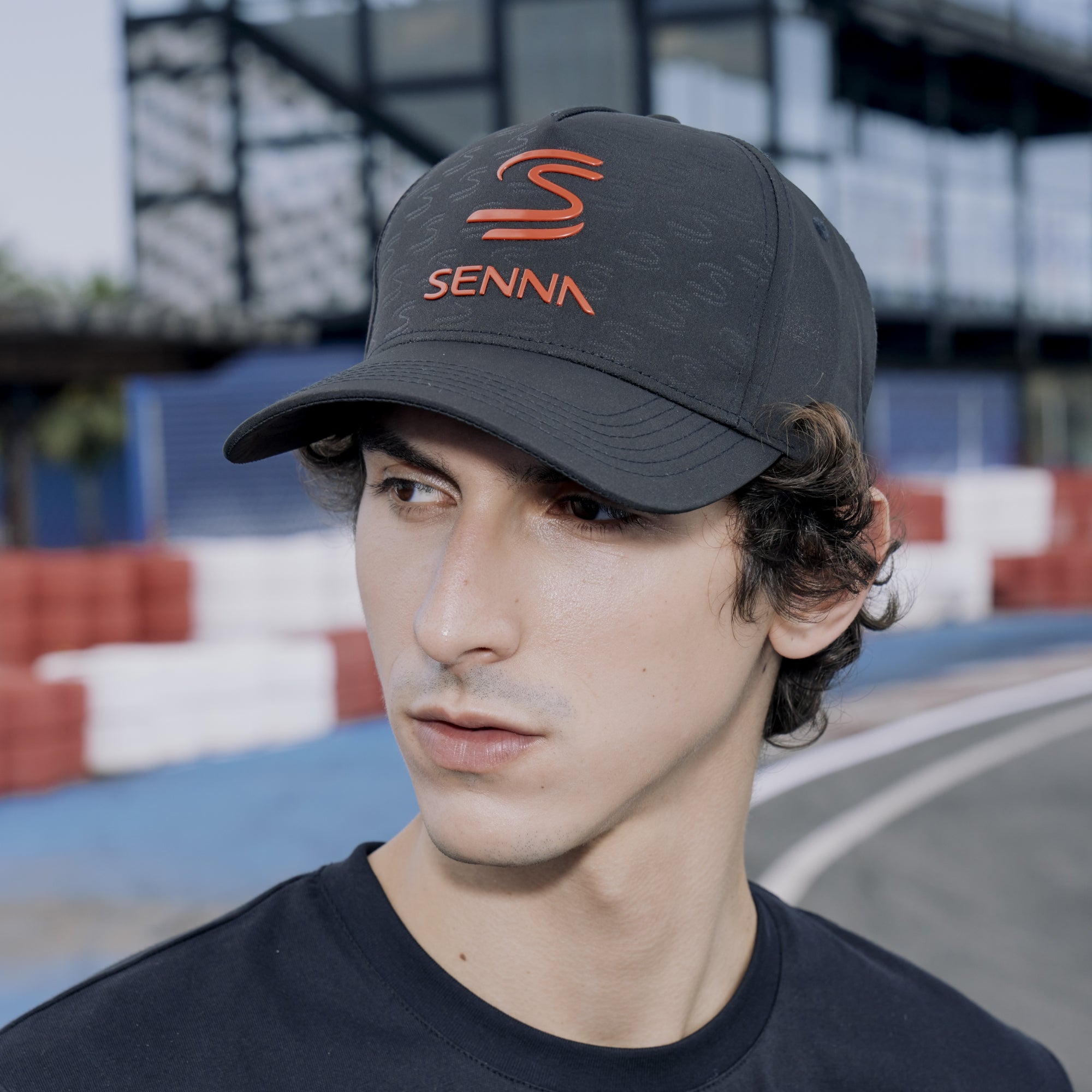 Person wearing a black cap with 'SENNA' branding on a race track background