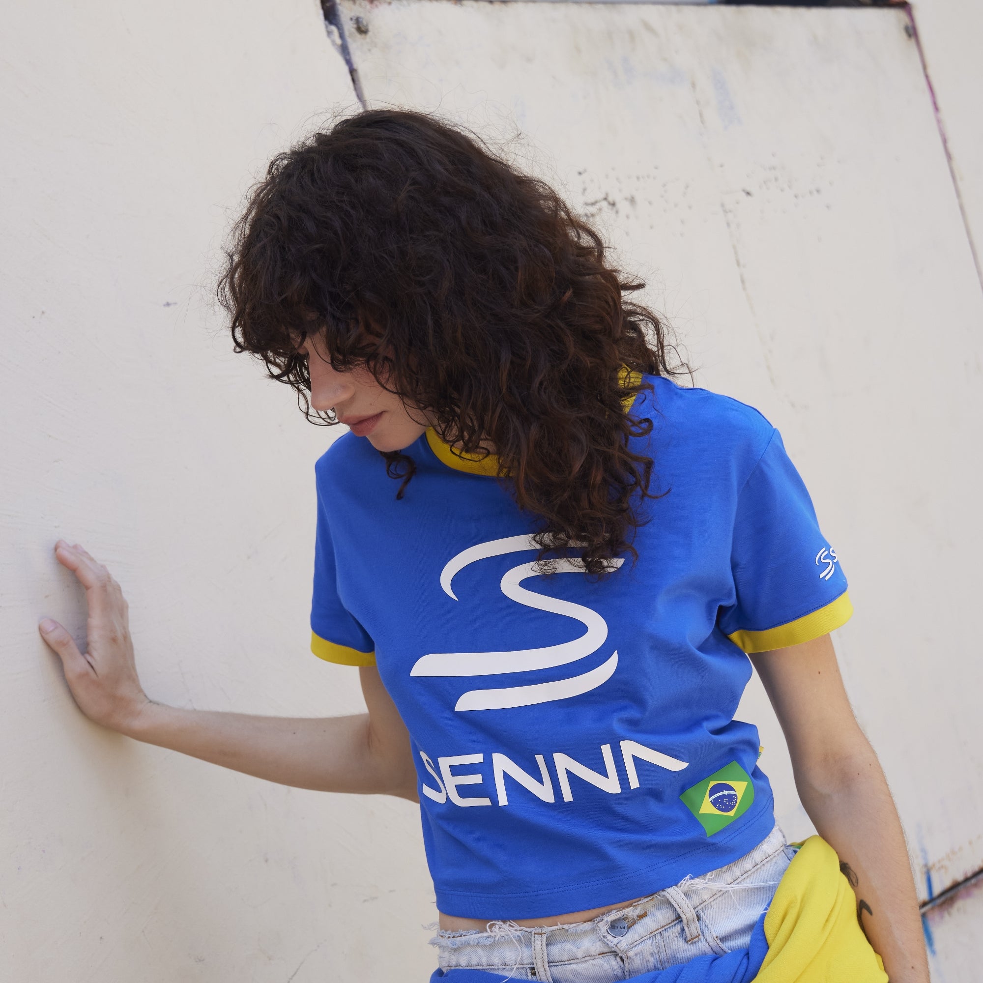 Person wearing a blue Senna shirt with a logo, standing against a light-colored wall.