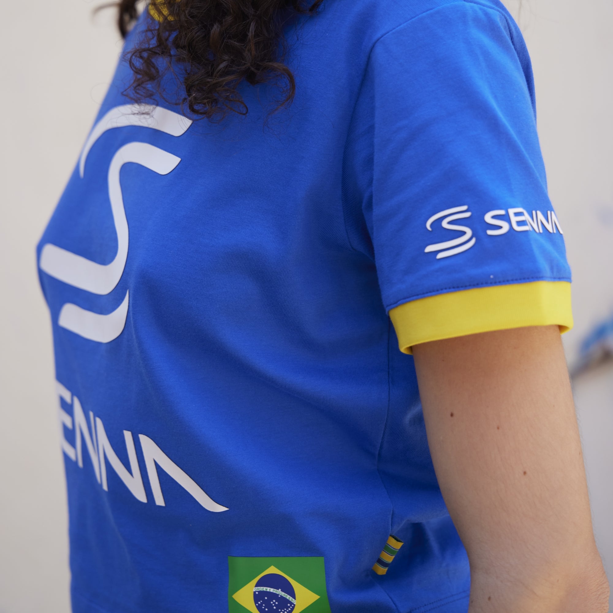 Person wearing a blue sports jersey with Senna branding and a Brazilian flag on a plain background