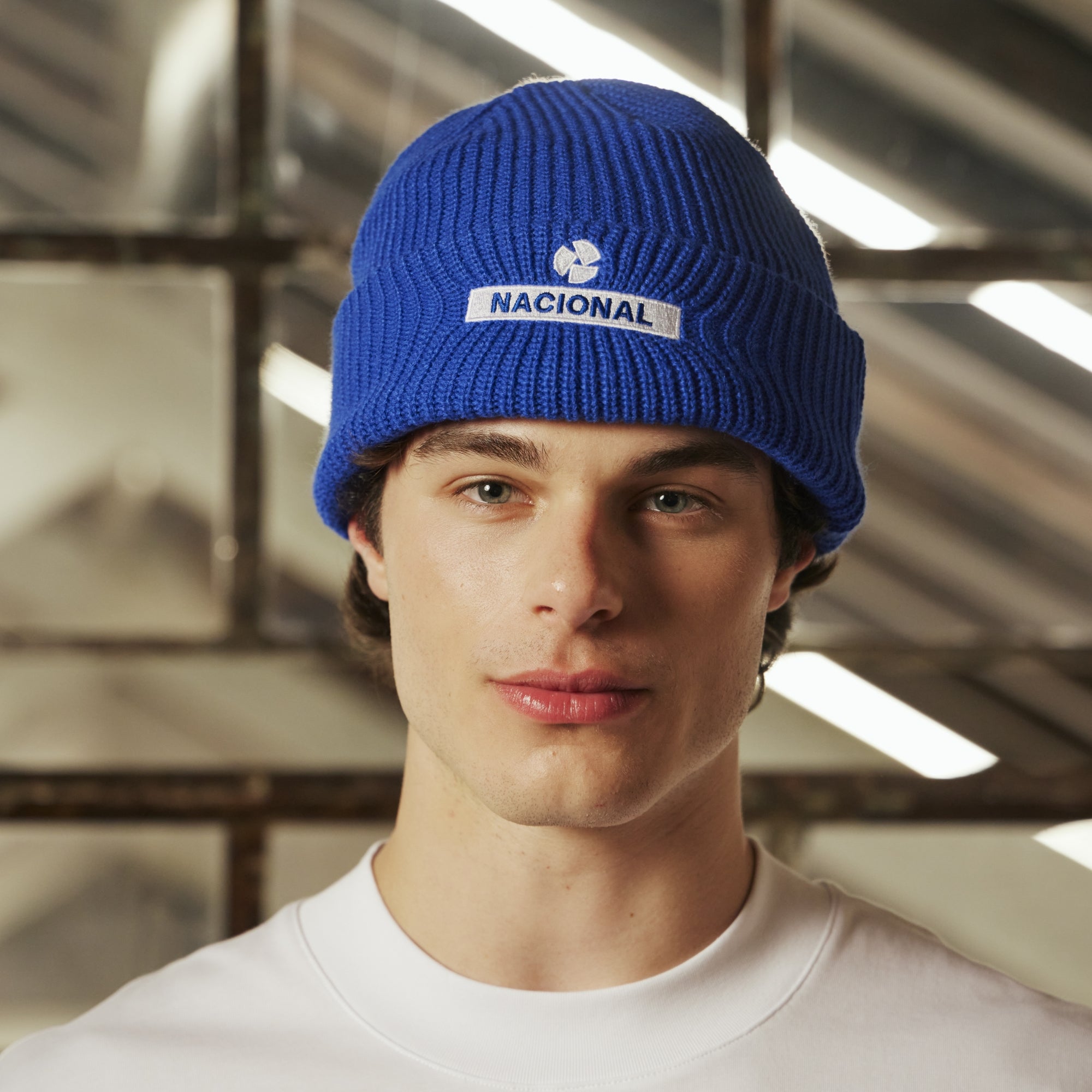 Person wearing a blue beanie with 'Nacional' logo against a metallic background