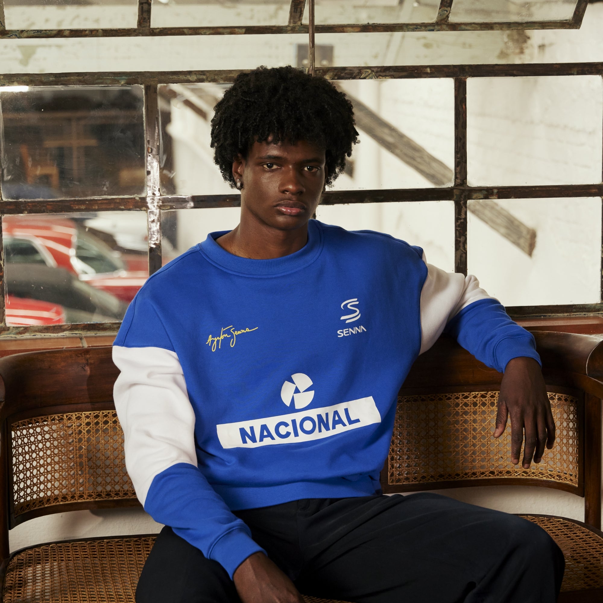 Person wearing a blue and white nacional sweatshirt with visible branding, sitting on a wicker chair.