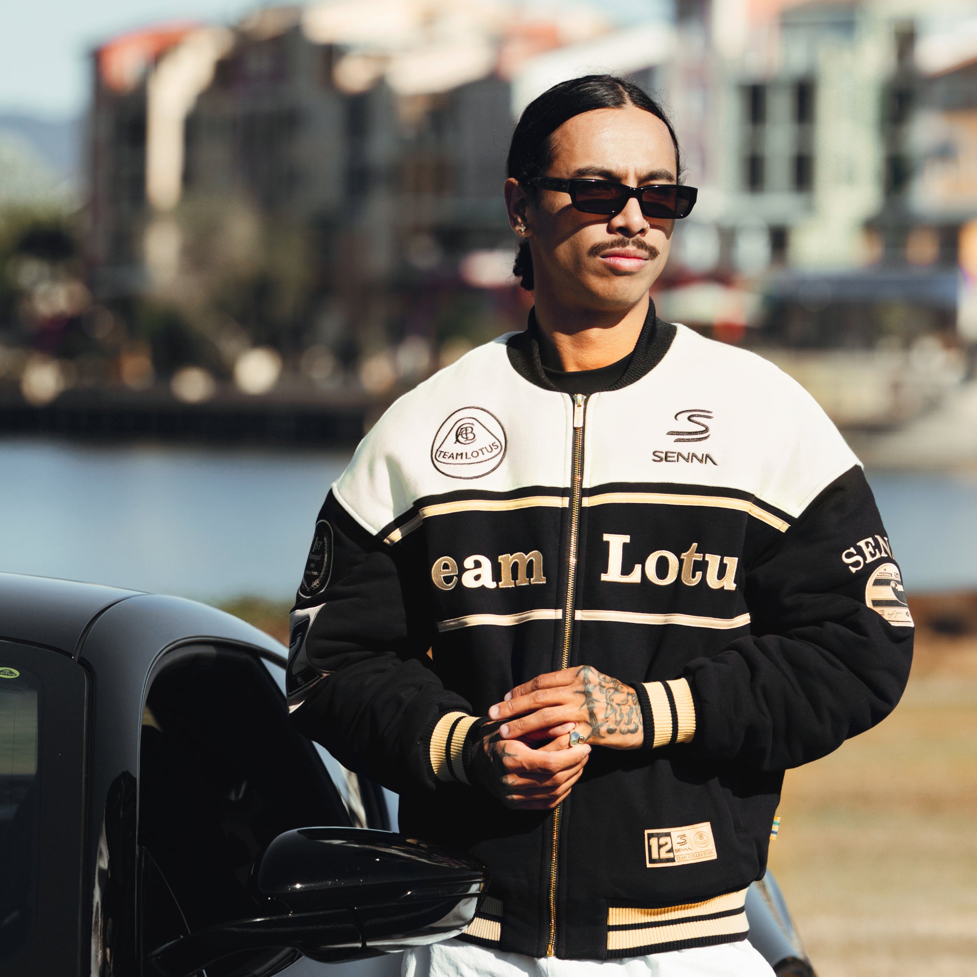 Front view of a male model wearing sunglasses and a black and white Senna Team Lotus varsity jacket.