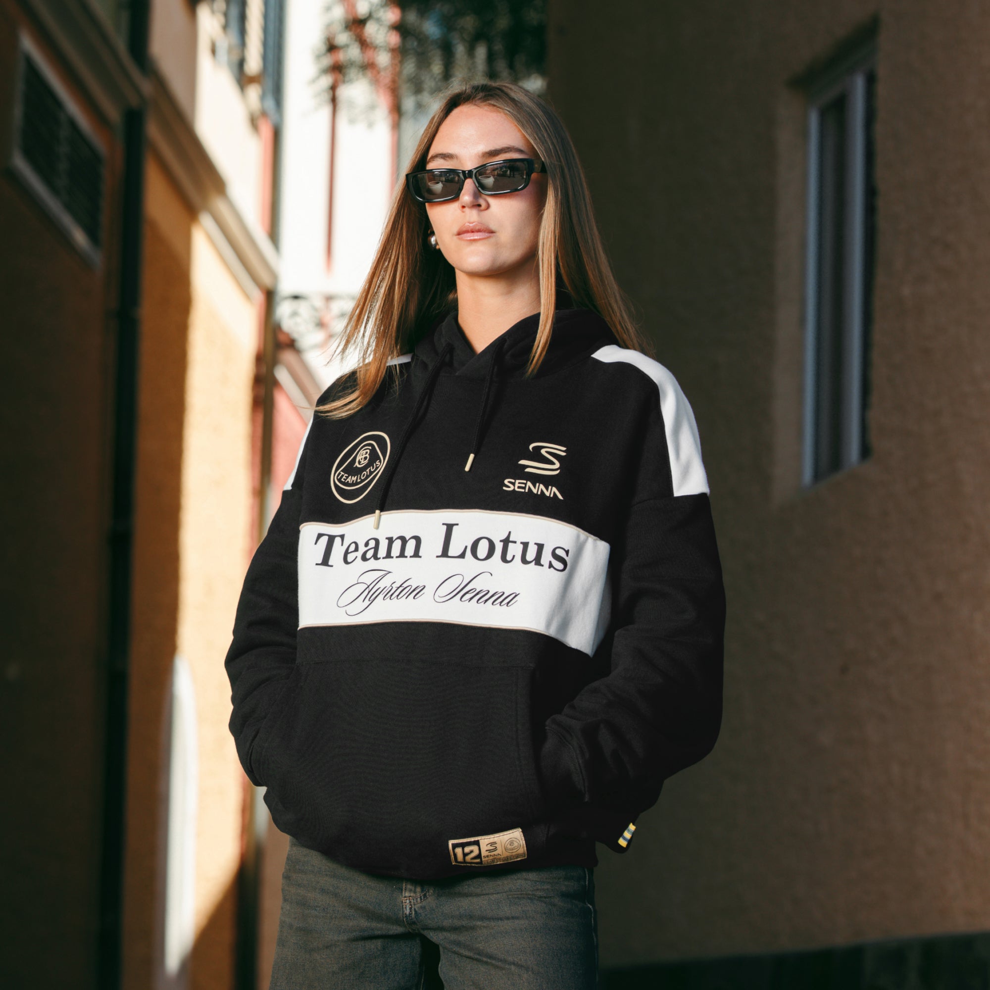 Female model wearing a black Team Lotus Ayrton Senna hoodie with her hands in the front pocket.