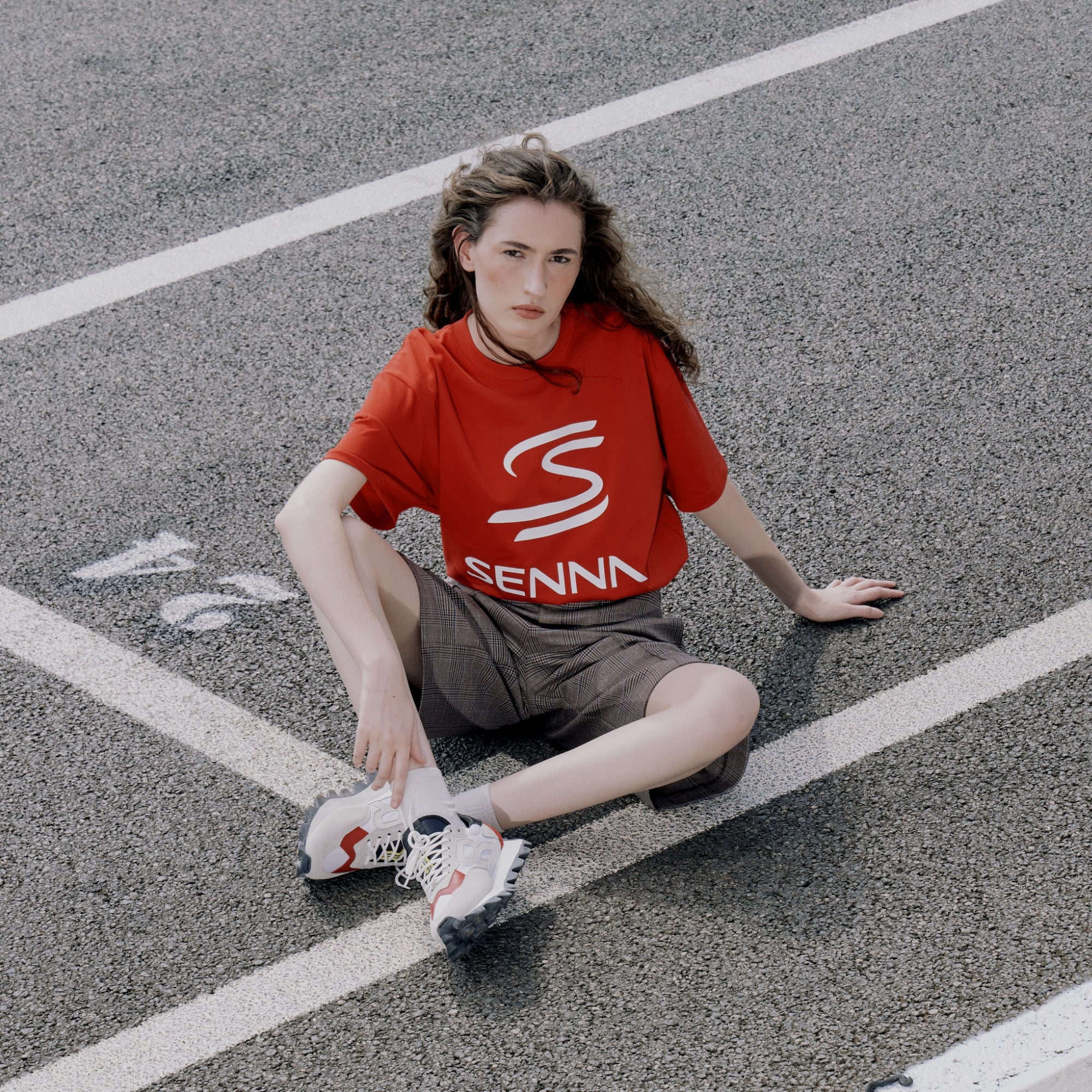 Person wearing a red tee with 'Senna' logo sitting on a road.