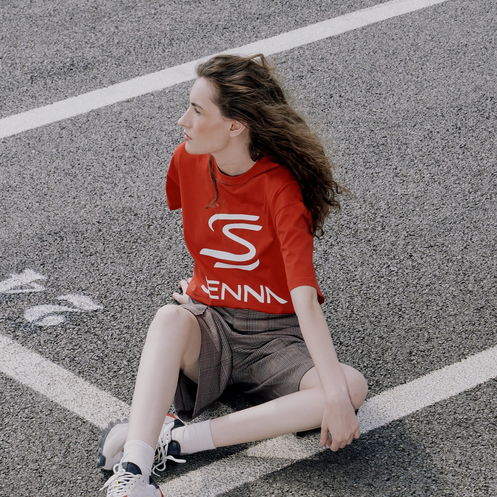Person wearing a red shirt with a white Senna logo sitting on a road.