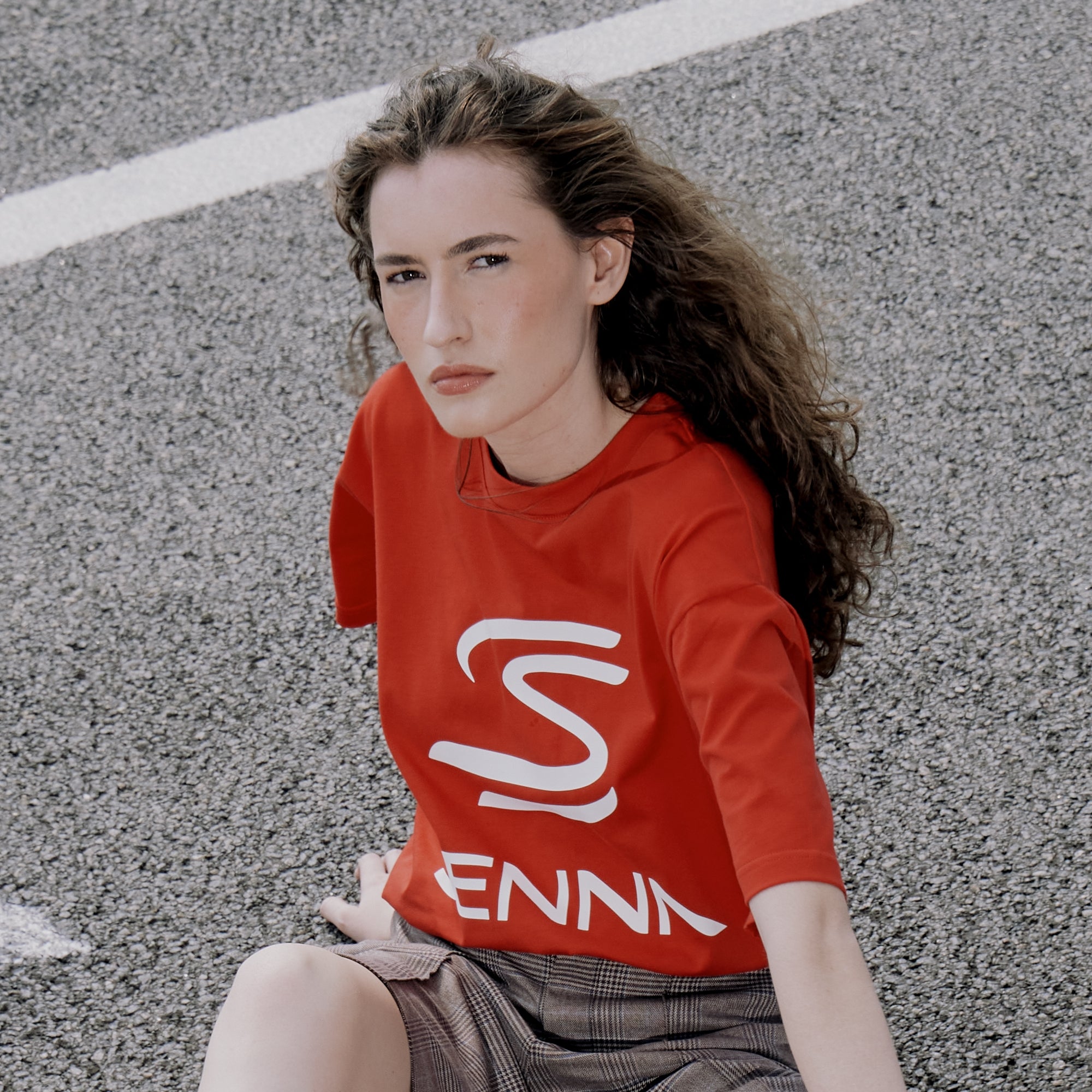 Woman wearing a red Senna relaxed fit T-shirt with a logo sitting on a street.