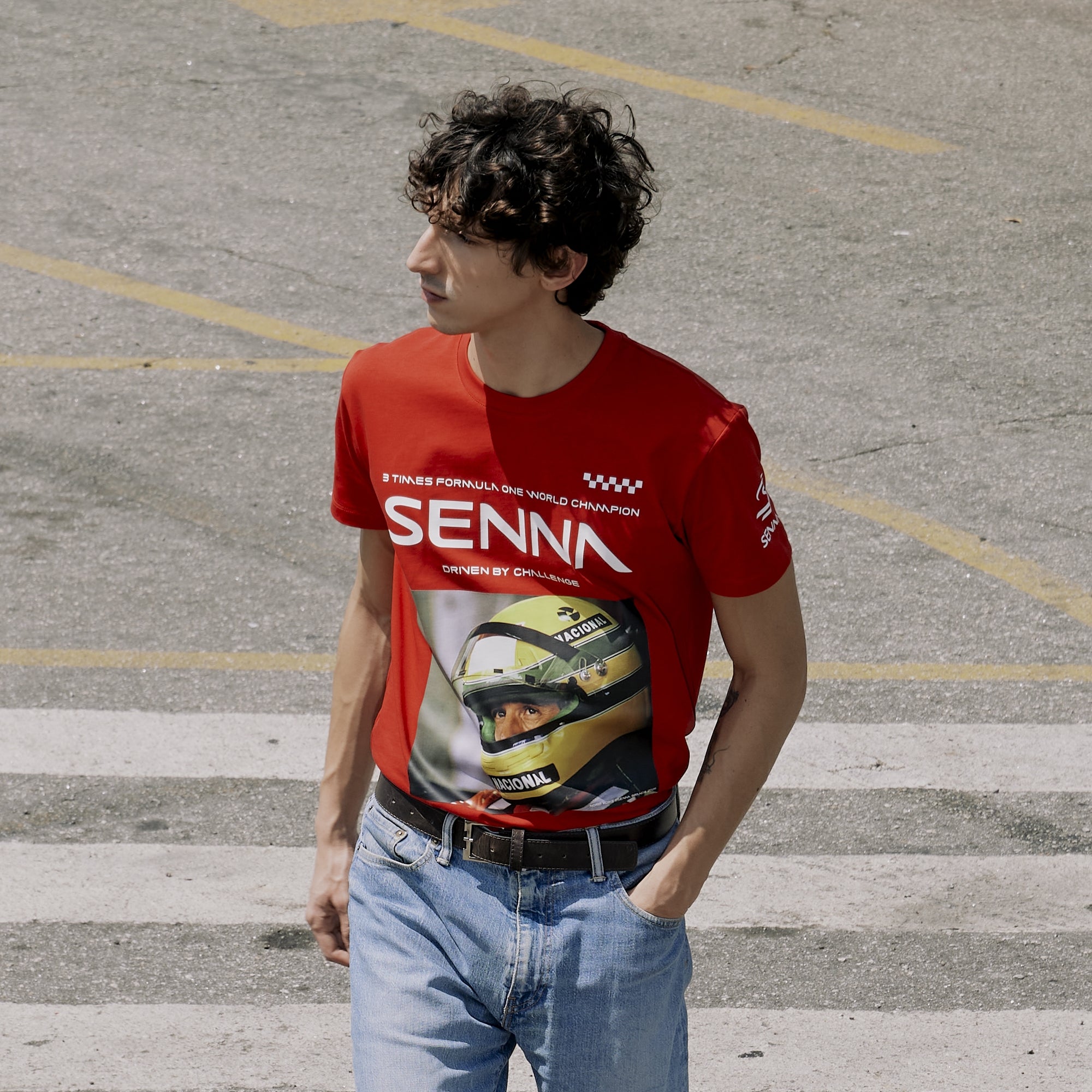 Person wearing a red 'Senna' t-shirt with a graphic of a helmet in an outdoor setting.