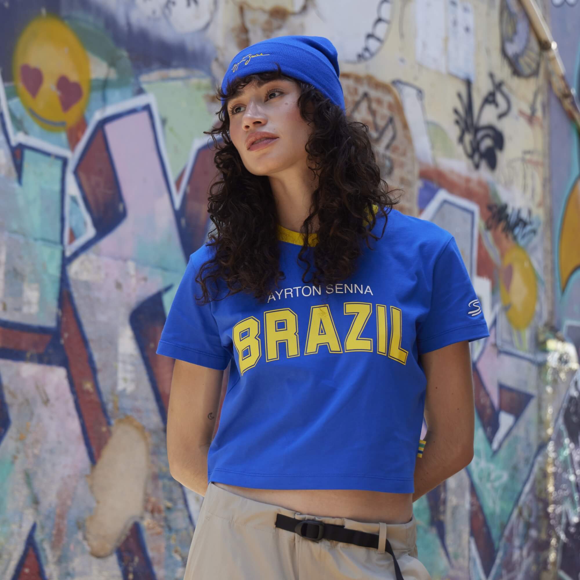 Woman wearing a blue 'BRAZIL' cropped t-shirt in front of a colorful graffiti wall.