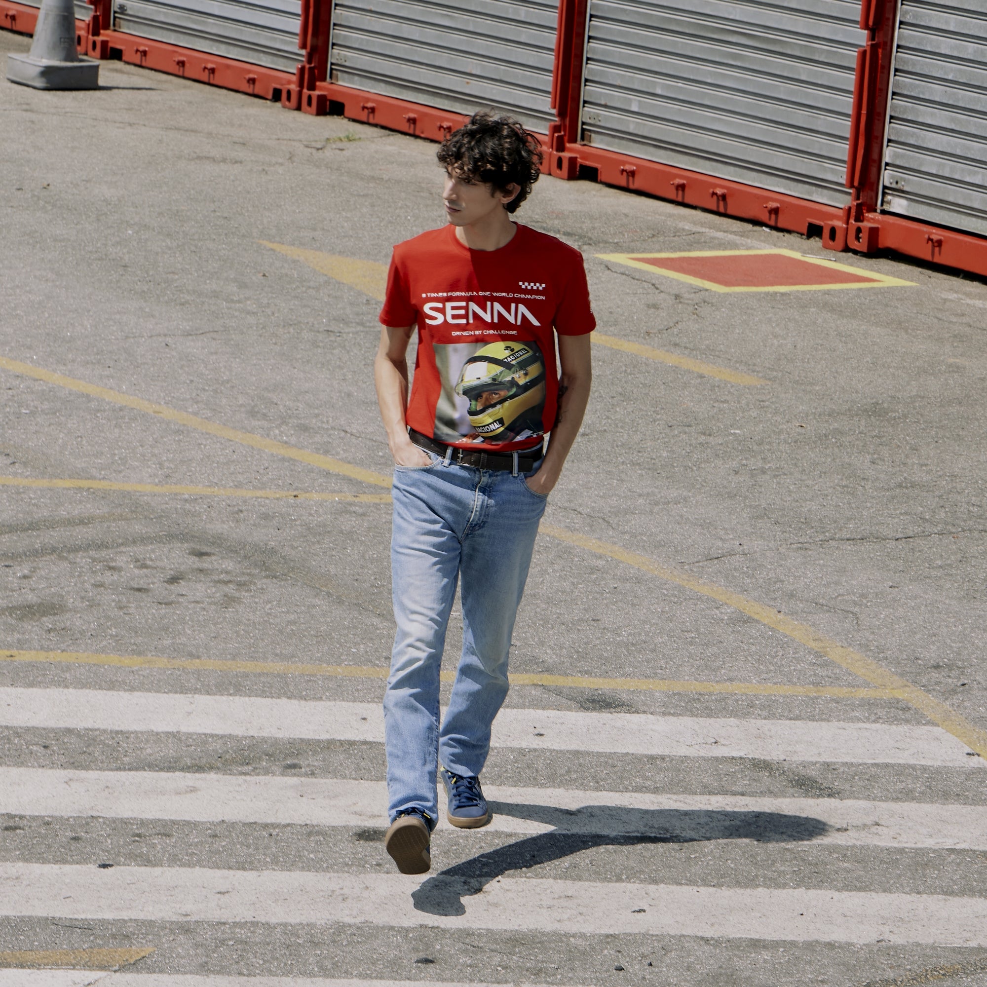 Person wearing a red 'SENNA' t-shirt with a graphic design, walking on a concrete surface.