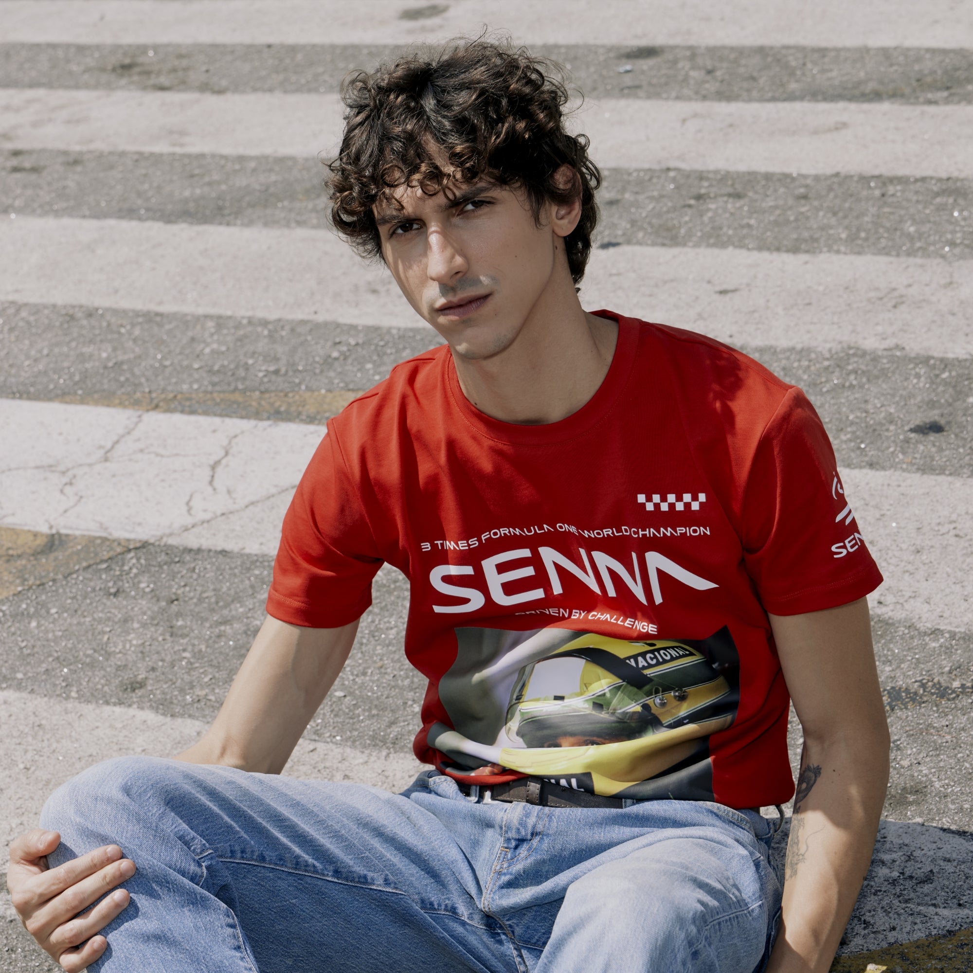 Person wearing a red Senna t-shirt sitting on a street.