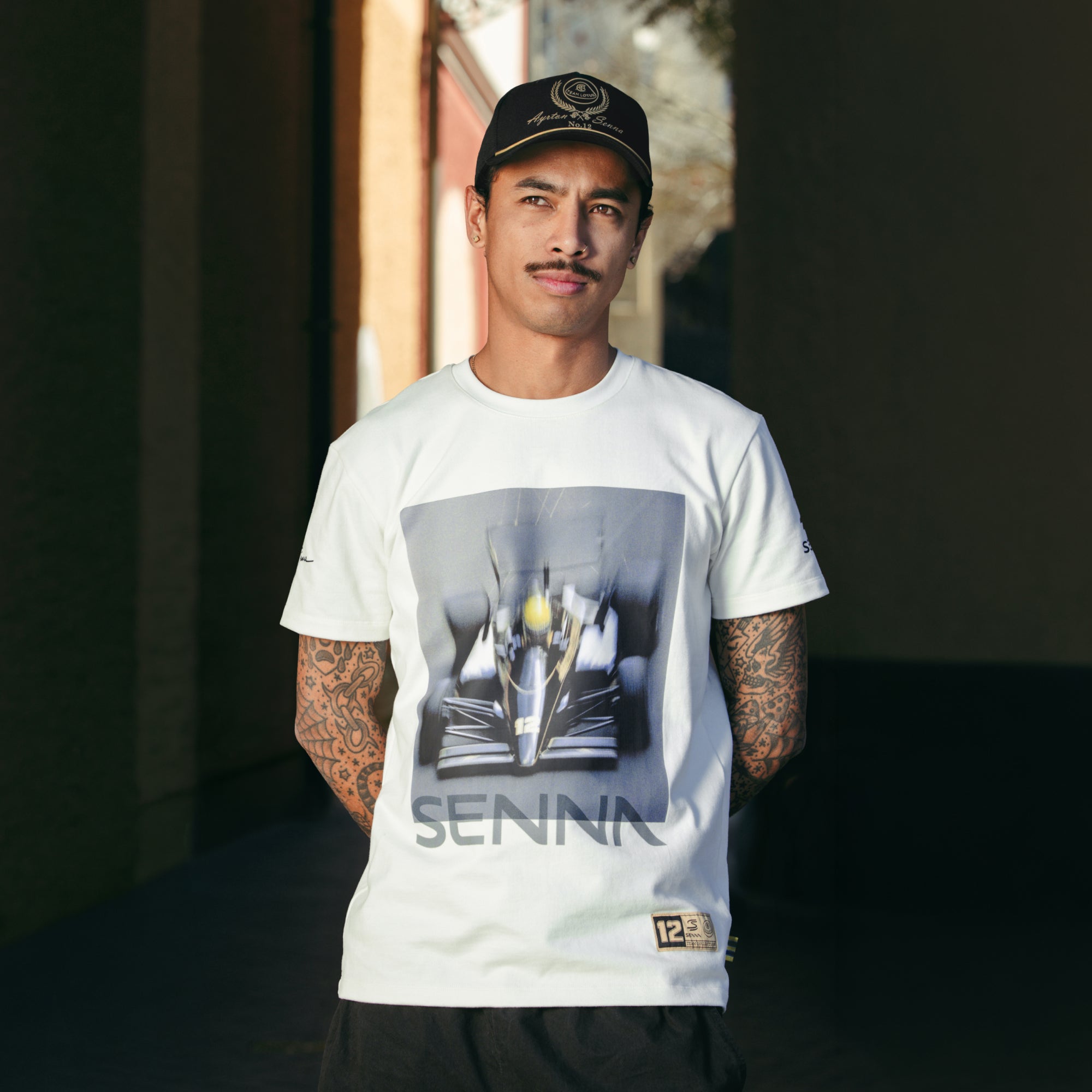 Man relaxed pose wearing a cream standard fit t-shirt with Formula 1 Senna Team Lotus race graphic print on front.